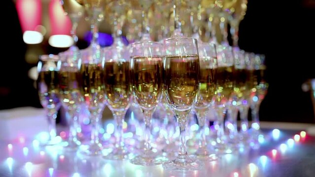 Pyramid of champagne glasses. The tower is undercut by bright lights. Full glasses of sparkling wine at a restaurant party. Holiday, wedding, birthday, event. Dry ice. Champagne with smoke
