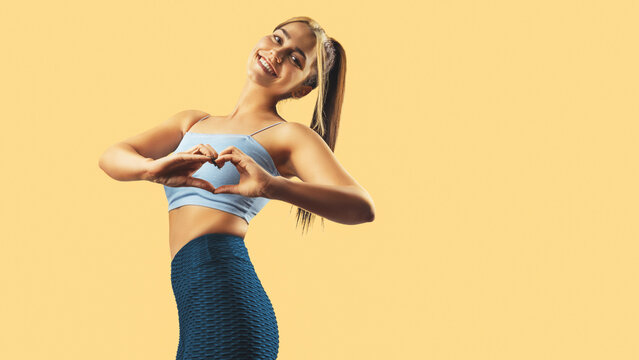 Beautiful fitness girl posing and showing heart with hands. Healthy body concept.