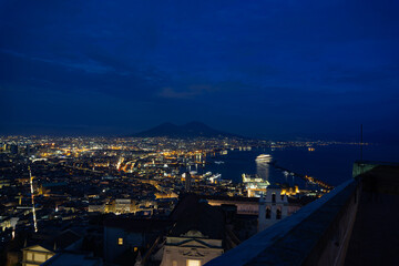 Panoramic view of Naples with Vesuvius in the background, the blue sky with clouds at sunset. City lights on with long exposure.