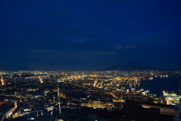 Panoramic view of Naples with Vesuvius in the background, the blue sky with clouds at sunset. City lights on with long exposure.