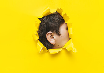 Close-up of a man's ear through a torn hole in yellow paper. The concept of eavesdropping,...