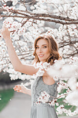 Portrait of pretty blong girl posing against the spring blooming trees in the garden.