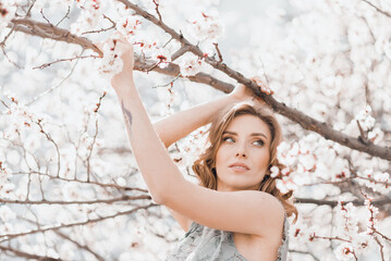 Portrait of pretty blong girl posing against the spring blooming trees in the garden.