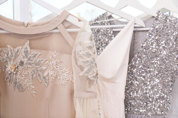 Hangers with different beautiful dresses in atelier, closeup