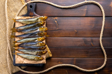 Smoked fish on a wooden cutting board on a dark wooden table. View from above, flat lay.