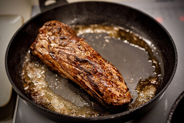A piece of beef is fried in a pan.