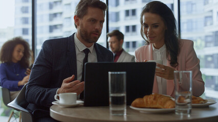 Focused business people discussing marketing using laptop computer in cafe.