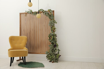 Stylish photo zone with wooden screen, floral decor and comfortable armchair indoors. Space for text