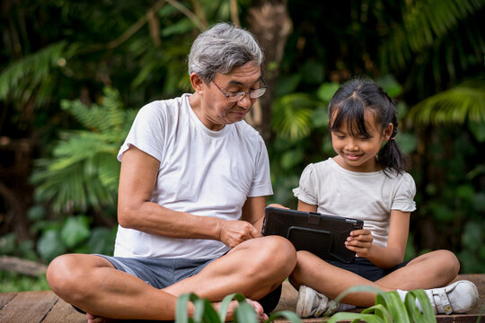 Happiness old man and little girl with digital tablet technology in park.