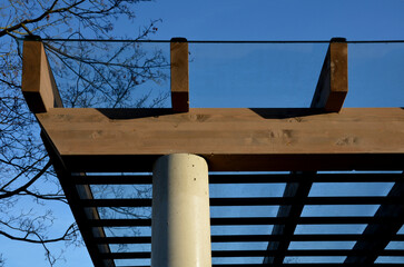 brown glued wooden structure of the pergola supported by smooth cylindrical white columns shelter...