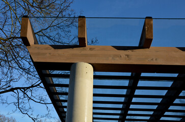 brown glued wooden structure of the pergola supported by smooth cylindrical white columns shelter...