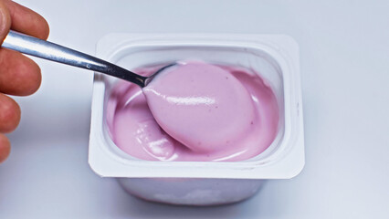 cropped view of man holding spoon near container with yogurt on white
