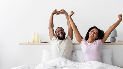 Glad happy young african american lady and guy woke up stretching body and enjoy morning