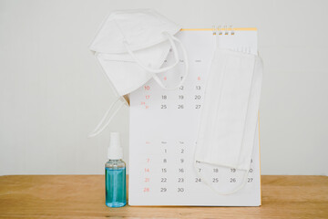 white face mask on white opened calendar and alcohol spray bottle on wooden desk,  for awareness of...