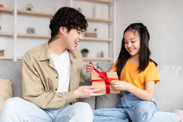 Satisfied japanese millennial father receives gift from teen daughter open box with gift in living room interior