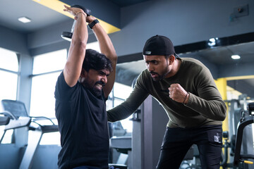 focus on client, Trainer motivating athlete to push his limits during workout at gym - concept of...