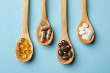 Wooden spoons with different dietary supplements on light blue background, flat lay