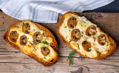Toasted sandwich from traditional sourdough bread with cheese and brown mushrooms seasoned with rosemary herb on a wooden board, top view