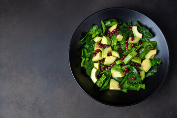 Avocado salad with spinach and pomegranate in a black plate on black background.
