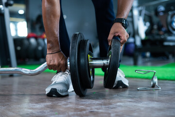 Focus on disc, close up shot hands adding weight to barbell rod at gym - concept of fitness...