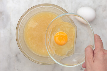 Hand holding raw egg in glass bowl
