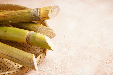 Sugar cane and green leaf in a wooden tray on a beige background, space for text.