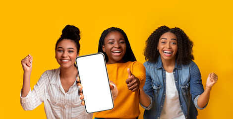Three emotional black ladies gesturing on yellow, showing cellphone, mockup