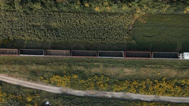 Long train with empty freight cars travels on rails of railway for heavy industrial goods. Field road. Empty wagons move on rails and sleepers to load them with fuel coal. Heavy industry. Top view.