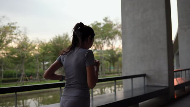 Happy slim woman wearing sportswear jogging in the city at sunrise. Young beautiful asian female in sports bra running outdoor. Workout exercise in the morning. Healthy and active lifestyle concept.