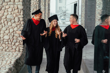 Fototapeta na wymiar Graduate friends in gowns walk along university corridor and talking excitedly