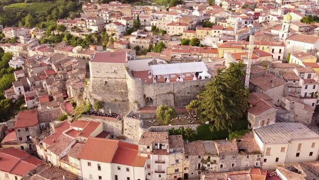 Aerial backwards view of an ancient castle, with wedding party set on terrace. Guardia Sanframondi. Italy. 
