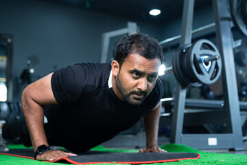 young indian athlet warming up by doing push ups at gym - concept of muscle or bodybuilding, fit...