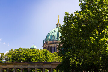 The architectural dome of Berliner Dom peeking up behind green trees during summer in Berlin Germany © Michael Persson