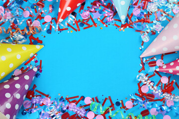 Obraz premium Frame of colorful serpentine streamers, party hats and confetti on light blue background, flat lay. Space for text