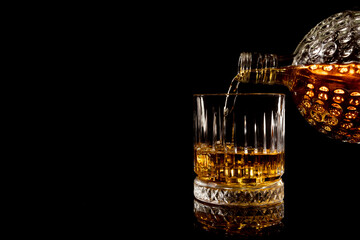 pouring glass of whiskey on black background