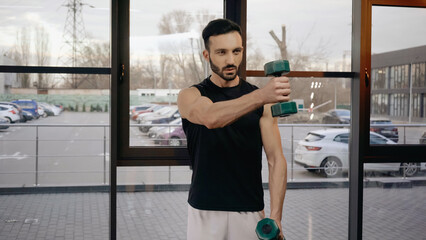 Athletic sportsman training with dumbbells in gym