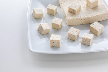 Tofu cut in cubes. Firm tofu on white plate. Vegan protein food.