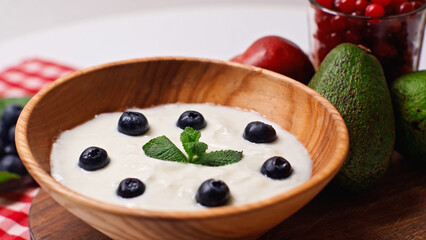 fresh fruits near wooden bowl with yogurt and blueberries on white
