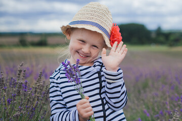 toddler girl in hat on lavender field smiling holding lavender and waving hand