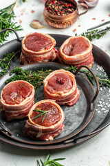 Raw beef filet Mignon steak on metel tray with pepper and salt, filet mignon. beef tenderloin steaks wrapped in bacon and thyme on white background. vertical image. top view