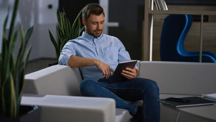 Serious businessman using tablet scrolling news information in modern office.