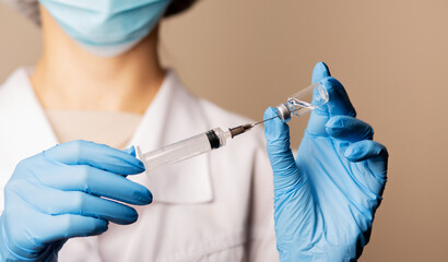 Female nurse in protective gloves filling a syringe with a vaccine