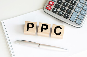 PPC text on wooden cubes on the background of a notebook on a table next to a pen and calculator