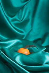 Tangerine fruit with leaf on blue green satin fabric. Minimal elegant artistic food concept