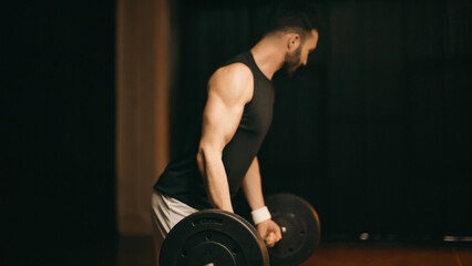 Blurred sportsman training with barbell on dark background