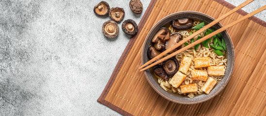 Asian vegan ramen soup with noodles, tofu cheese and shiitake mushrooms in a bowl on a bamboo mat....