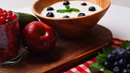 fresh fruits, peppermint and berries near wooden bowl with yogurt on white