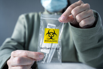 Person with facial mask are holding biohazard bio safety bag with used antigen test car kit inside.