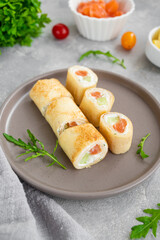 Thin pancake rolls or crepes rolls with smoked salmon, cream cheese, cucumber and dill on a gray concrete background. Selective focus.