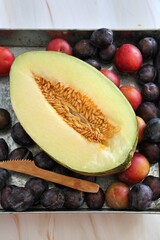fresh summer fruit on a metal plate, purple oblong plums and round red-orange plums, yellow melon cut in half, healthy food, juicy melon, melon seeds
